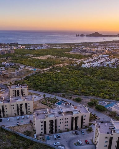Aerial view of modern residential complex at sunset overlooking coastal town, ocean, and distant rocky islands