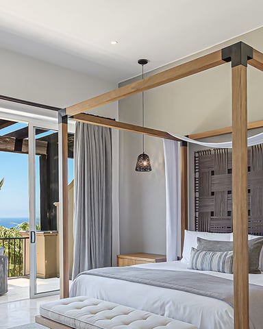 Luxury bedroom with wooden canopy bed, ocean view through glass doors, and palm trees on terrace