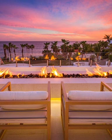 Beachfront fire pit lounge at sunset with wooden chairs, palm trees, and Mediterranean hillside buildings