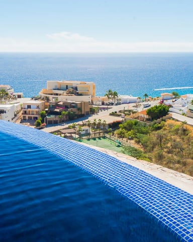 Infinity pool overlooking Mediterranean coastal village with colorful buildings and blue sea