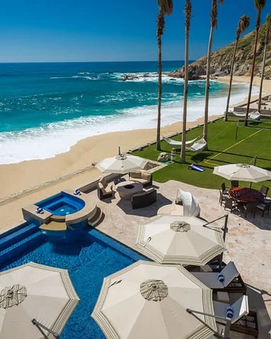 Beachfront property with infinity pool, lounge umbrellas, palm trees, and turquoise ocean view
