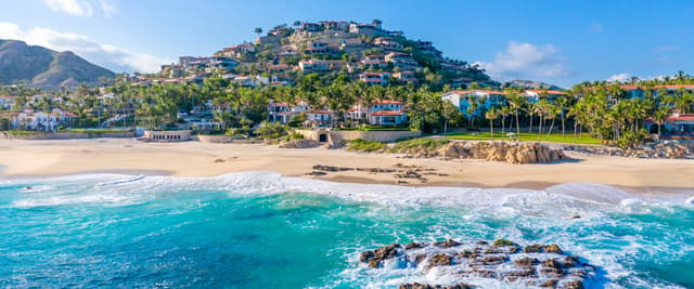 Comunidad en una ladera frente al mar, con casas coloridas, palmeras, una playa de arena y olas de color turquesa