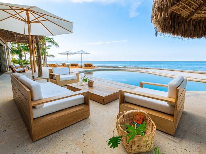 Beachfront terrace with wooden lounge chairs, infinity pool, umbrellas, and ocean view